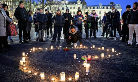 People stand around a collection of candles placed on the ground in the shape of a heart