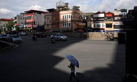 A man carries an umbrella to shade from the sun along a street in Hanoi.