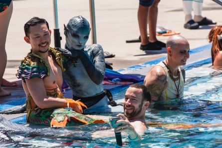 Three people in merfolk cosplay sit by the pool.