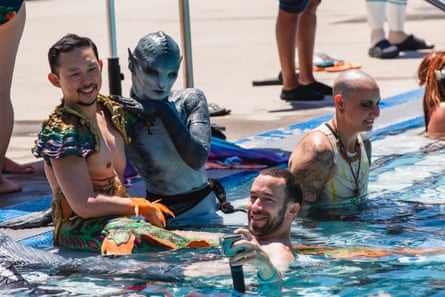 Three people in merfolk cosplay are sitting by the pool.