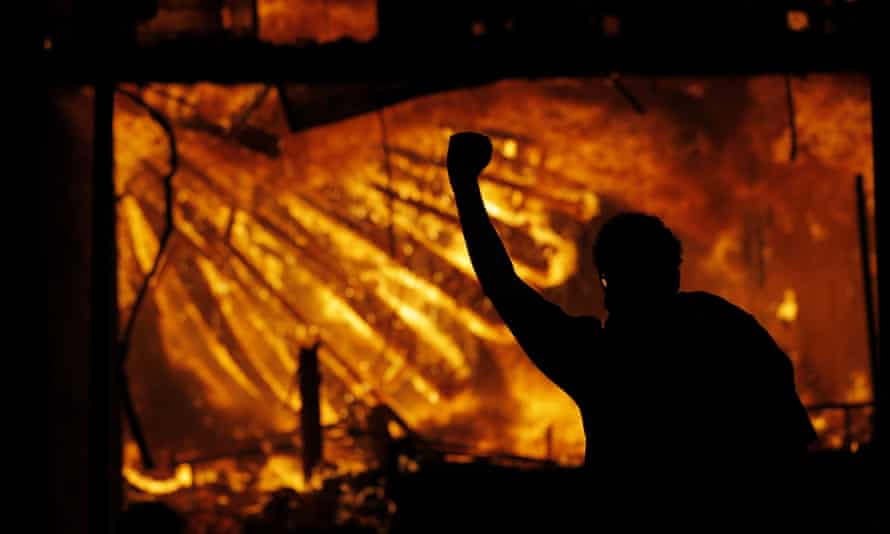 In this May 28, 2020 file photo, a protester gestures in front of the burning 3rd Precinct building of the Minneapolis Police Department in Minneapolis
