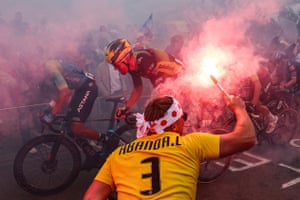 Team Visma - Lease a Bike team’s Tiesj Benoot and the peloton passes a flare waving spetator past a spectator waving a flare in an ascent in the final kilometres of the stage.