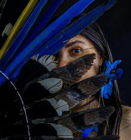 Priscila Tapajowara looking out from behind an arrangement of bright feathers