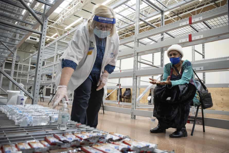 Gretchen Leider, Walmart’s vision center manager, picks up a bottle of water for Alice Collins while she is under observation after receiving the Moderna COVID-19 vaccine at a Walmart in the Austin neighborhood, of Chicago, Tuesday, Feb. 2, 2021. (Pat Nabong/Chicago Sun-Times via AP)