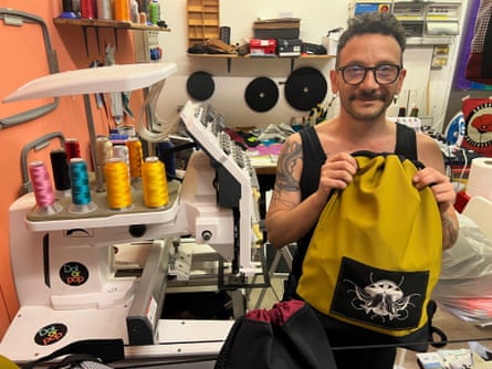 A man surrounded by sewing equipment holds up a bag