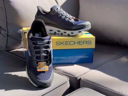 Grey and navy blue Skechers glover slip on shoes next to box on couch