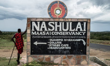 A young Maasai man leans against a sign in a savannah saying 'Nashulai Maasai conservancy – conserve wildlife, preserve culture, reverse poverty'