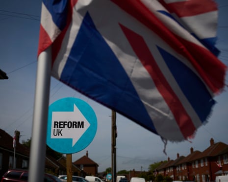 A Union Jack flag flies above a Reform UK sign with an arrow on a residential street
