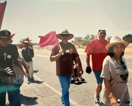 An older woman in a straw hat marches with other people holding red flags.