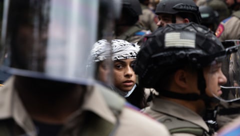 Young person in keffiyeh surrounded by officers in riot gear