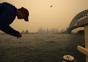 The Sydney Harbour Bridge seen through smoke haze from bushfires as a man fishes from a pier during hot weather in Sydney