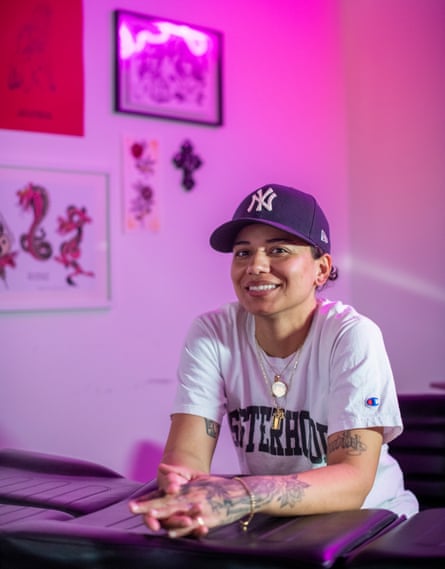 Cake in her studio, with pink lighting, wearing a baseball cap and a white T-shirt with ‘sisterhood’ on it, showing her tattooed forearms