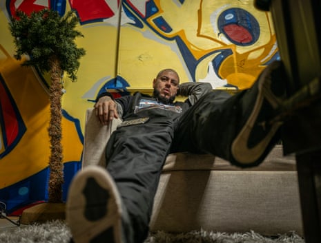 Man relaxes as he sits in front of a graffiti-covered wall at a boxing gym.