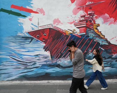 People walk past a mural depicting a US aircraft carrier under missile attack in Tehran on Sunday