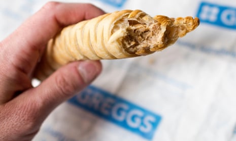 A person holding a Greggs vegan sausage roll with a bite out of it.