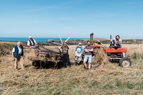 Seven members of the Llafur Ni network, including Gerald Miles, Iwan Evans and Owen Shiers, smile as they stand next to or sit on a reaper-binder and tractor in a field