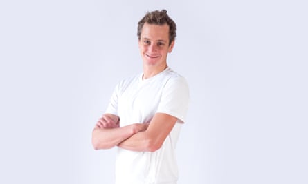 A smiling Alistair Brownlee poses for a photo with his arms crossed in a white tshirt against a white background