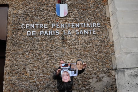 A person holds a poster with cutout images of Nicolas Sarkozy and Marine Le Pen outside La Santé prison