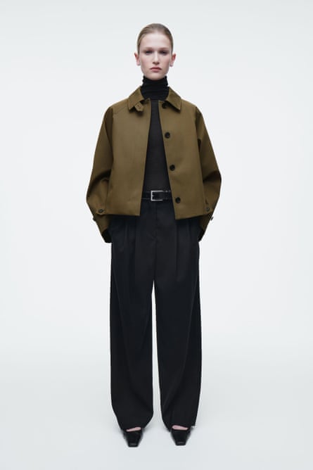 A model wearing a khaki cropped trench coat and black trousers