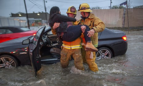 A firefighter carries a woman from her car after it was caught in street flooding.