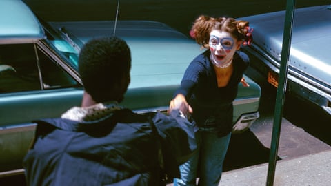 A clown performer interacting with someone between cars, photographed by Albert Scopin-Schoepflin