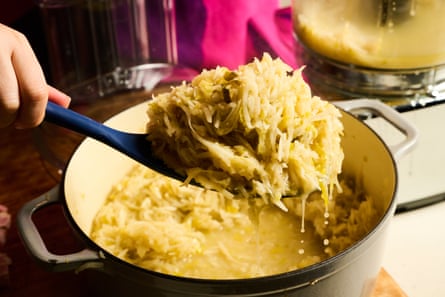 A hand holding up a spatula full of grated parsnip and chopped leek that has been cooked with cider in a pan
