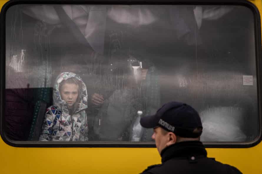 A police officer looks on as a girl from Mariupol looks out the window of a bus after a convoy of vehicles arrived at an evacuation point, carrying people from Mariupol, Melitopol and surrounding towns to Zaporizhzhia.