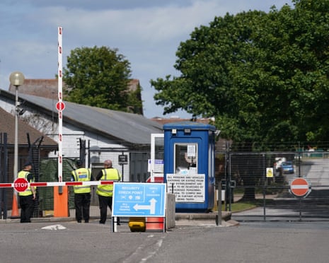 Three people in hi-vis jackets standing by barriers at a security check point