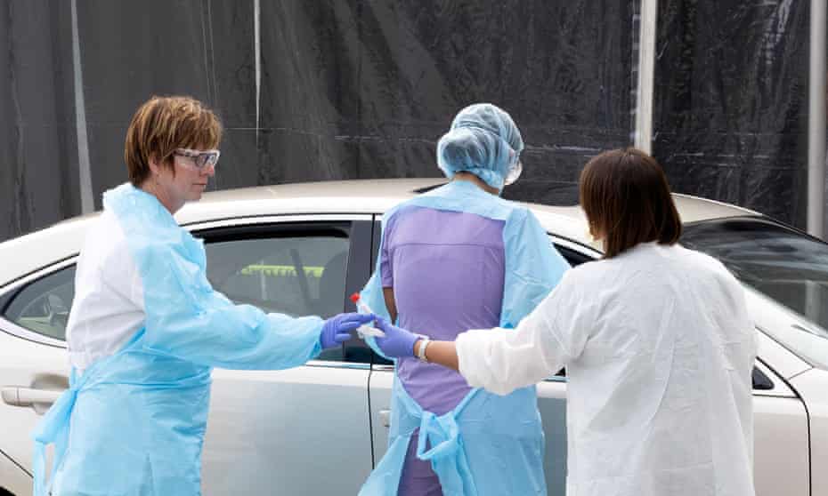 Healthcare personnel receive a swab sample of a person to be tested for the coronavirus in a drive up tent in the parking lot of Kaiser Permanente medical center in San Francisco.