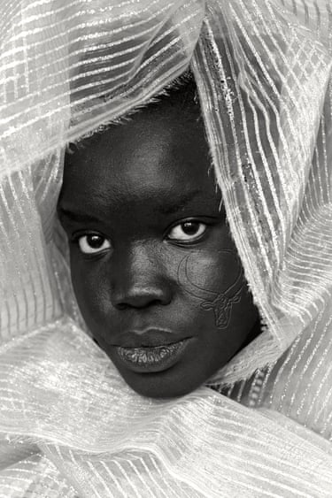 Close-up portrait of a woman wrapped in sheer fabric, with a cow-shaped scar on her cheek