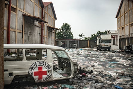 A van and a truck marked with the International Committee of the Red Cross (ICRC) logos lie between warehouses with plastic bags and other rubbish all over the ground