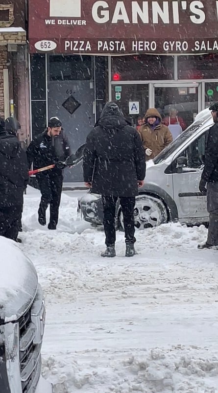 Man with shovel in hand while others stand around SUV on showy road