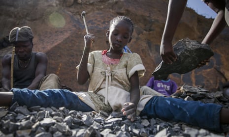A young girl sits breaking rocks with a hammer in a quarry