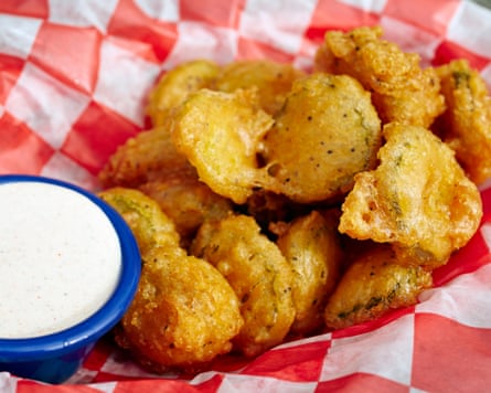 A basket of battered, deep-fried pickles sits beside a small bowl of creamy dip