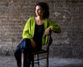 Imani Thompson in a bright green cardigan sits on a chair against an exposed brick wall.