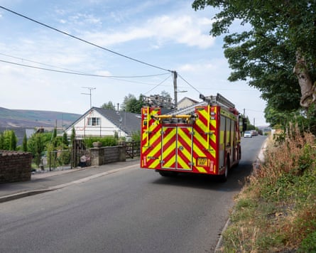 A fire engine drives along a road passing houses