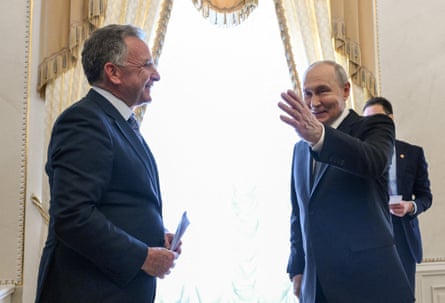 Putin waves and smiles while walking past Steve Witkoff in a grand palace room
