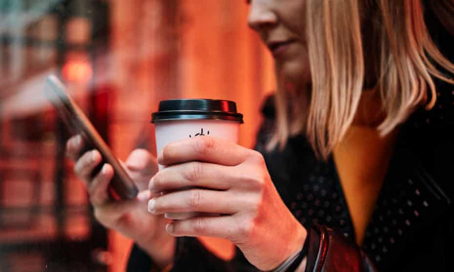 A woman holds a cup of coffee and a smartphone in a cafe