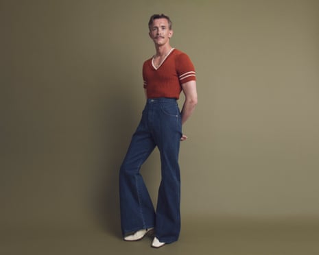 Stephen Libby waring high-waisted flared jeans, white boos and a rust short-sleeve V-neck knit.