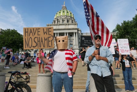 people protesting and holding signs and an American flag in front of a building