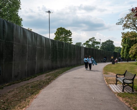 People walk past a high metal fence in a park
