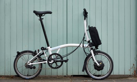 An electric Brompton standing against pale blue wooden cladding