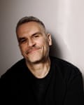 A man with a mustache wears a black shirt and smiles at the camera