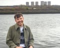 Musician Jamie Livingstone laughs beside water with buildings behind him