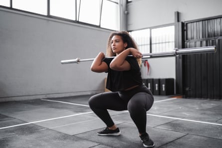 A woman holds a squat position with a barbell across her chest.