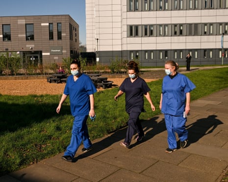 Three people in protective medical gear walking in front of university buildings