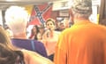 Woman speaks into microphone with Confederate flag in background
