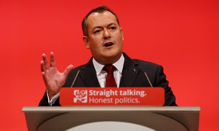 Michael Dugher standing at a lecturn with a red background