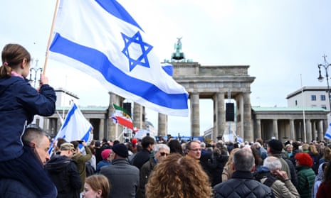 A girl sitting on a man's shoulders holds up an Israeli flag in Berlin, with the Brandenburg Gate in the background