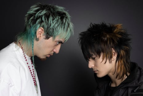 Man with blue hair and man with black hair styled in scruffy feathered hairdo face each other
